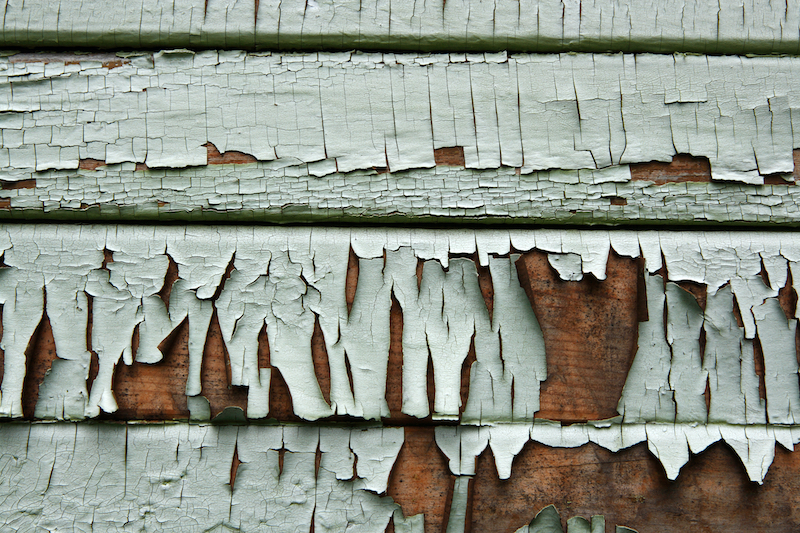 A close-up shot of a wood sided house with fading paint