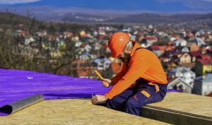 A picture of a roofer constructing new roof. Builder roofing surface. Professional master repair roof. Flat roof installation. Construction building. Waterproof sheet materials. High altitude works. Heat insulation