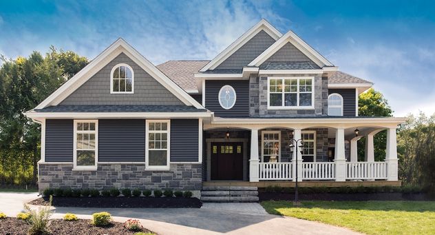 A wide front facing picture of a grey house with a large yard