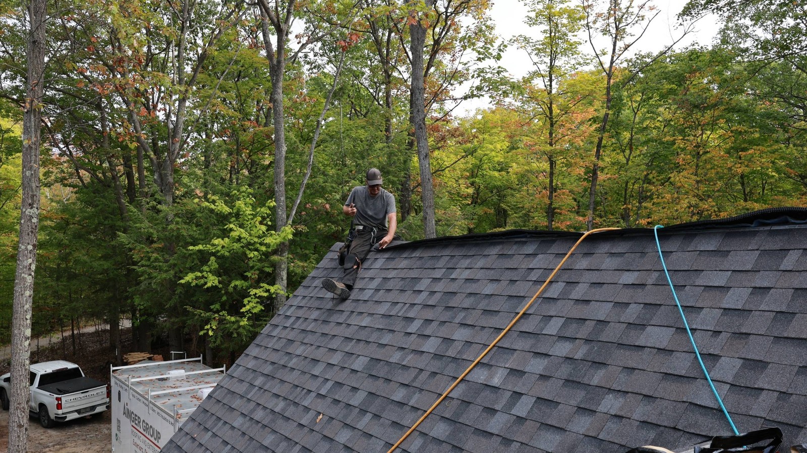 Ainger Group roofer working on a shingle roof surrounded by fall trees in Orillia.