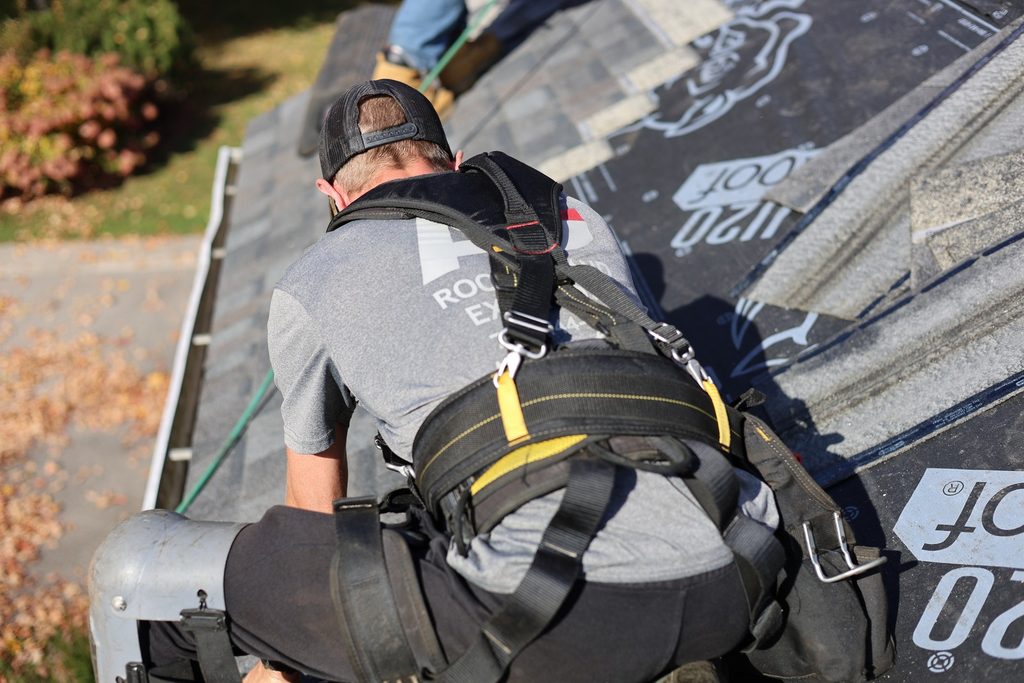 Harnessed Ainger Group roofer examining shingle installation details on a residential roof.